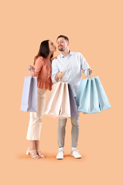 Ευτυχισμένο νεαρό ζευγάρι με τσάντες για ψώνια σε μπεζ φόντο - Φωτογραφία, εικόνα