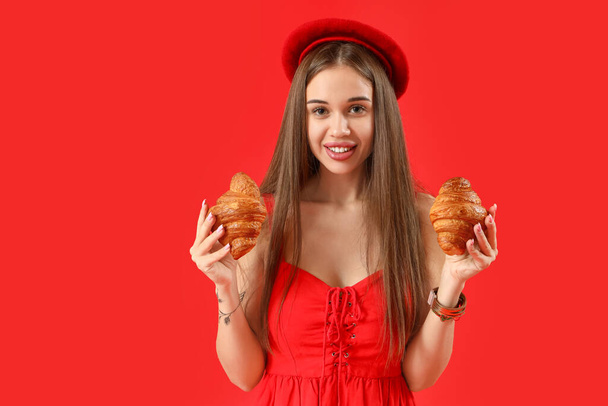 Schöne junge Frau in Baskenmütze mit leckeren Croissants auf rotem Hintergrund - Foto, Bild