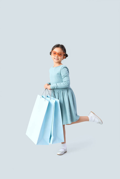 Cute little girl with shopping bags on light background - Foto, imagen