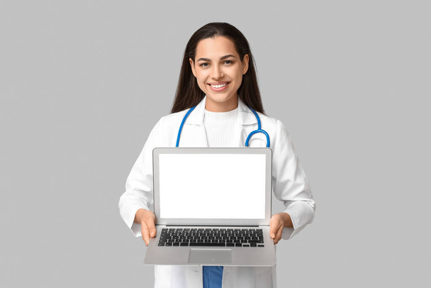 Retrato de médico do sexo feminino segurando laptop com tela em branco no fundo cinza - Foto, Imagem