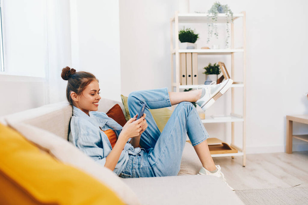 Smiling Woman Holding Mobile Phone on Cozy Sofa in the Living Room - Photo, Image