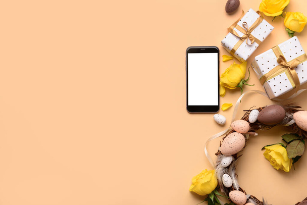 Komposition mit modernem Handy, Geschenken und Osterkranz auf farbigem Hintergrund - Foto, Bild