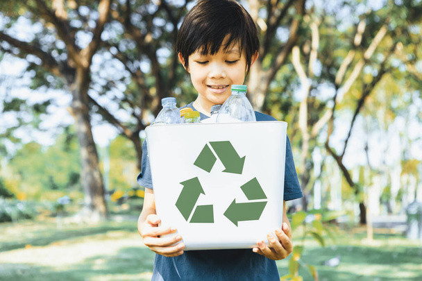 Wesoły młody azjatycki chłopiec trzymający kosz na symbole recyklingu w świetle dziennym naturalny zielony park promujący recykling odpadów, zmniejszający i ponownie wykorzystujący zachętę do ekologicznej zrównoważonej świadomości dla przyszłego pokolenia. Żywica - Zdjęcie, obraz