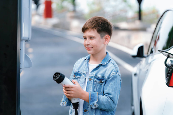 EV充電ステーションから環境に優しい電気自動車を充電する小さな少年. EVカーロード旅行コンセプト クリーンな再生可能で持続可能なエネルギーを駆使した代替輸送. パーペチュアル - 写真・画像