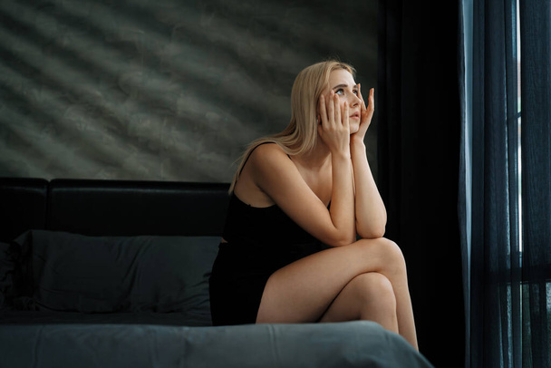 Молода жінка з критичною депресією і тривожним розладом від самотності, психічних захворювань або небажаної вагітності, присідає на темній спальні. Переважна негативна думка. Блайт - Фото, зображення
