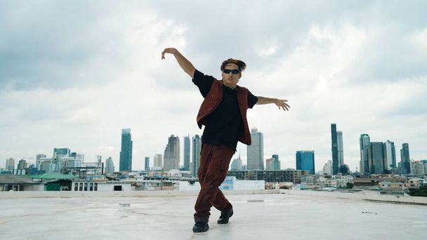 Motion shot z B-boy dance przez profesjonalnego ulicznego tancerza na dachu z scrapper niebo, widok na miasto. Atrakcyjny azjatycki hipster pokazuje energiczny krok. Sport na świeżym powietrzu 2024. Endeavor. - Zdjęcie, obraz