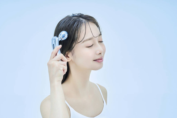 Young woman self-massaging her face and pale blue background - Photo, Image