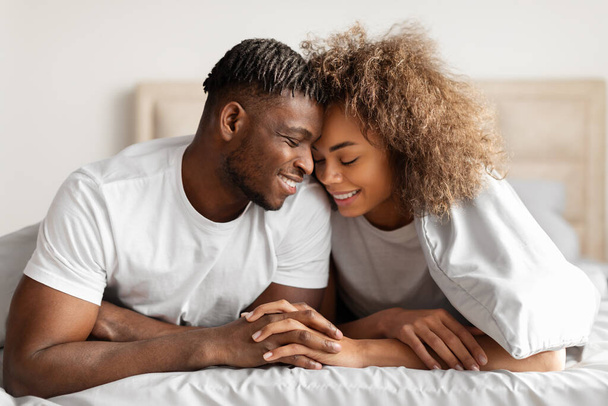 アフリカ系アメリカ人の若いカップルを愛し,手を保持し,外見に触れる,快適なベッドでカドリングと浮気,ベッドルームのインテリアで親密さとロマンスを楽しむ - 写真・画像