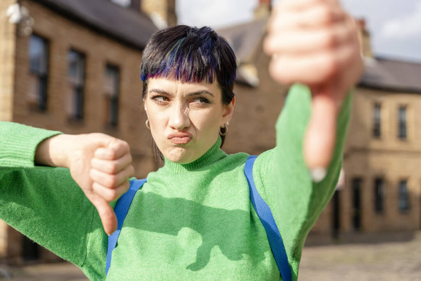 woman in green sweater giving thumb down gesture, dislikes something, having disgusting expression, showing disapproval sign outside Negative human expression and body language concept. - Photo, Image