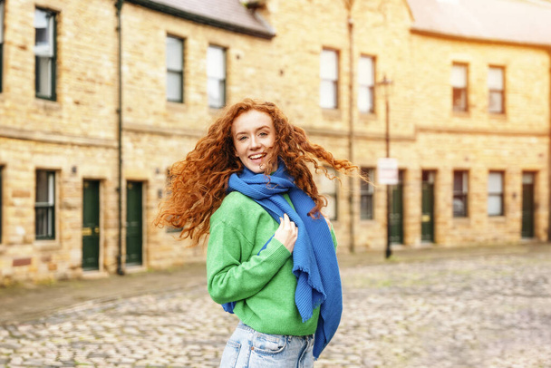 Tatildeki neşeli, genç, kızıl saçlı bir kadın. Yeşil bir kazak giymiş sırt çantalı bir turist eski bir Avrupa şehrinde geziyor.. - Fotoğraf, Görsel