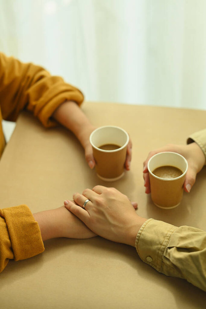 Νεαροί εραστές που πίνουν καφέ κρατώντας τα χέρια τους. Έννοια αγάπης, σχέσης και τρόπου ζωής. - Φωτογραφία, εικόνα