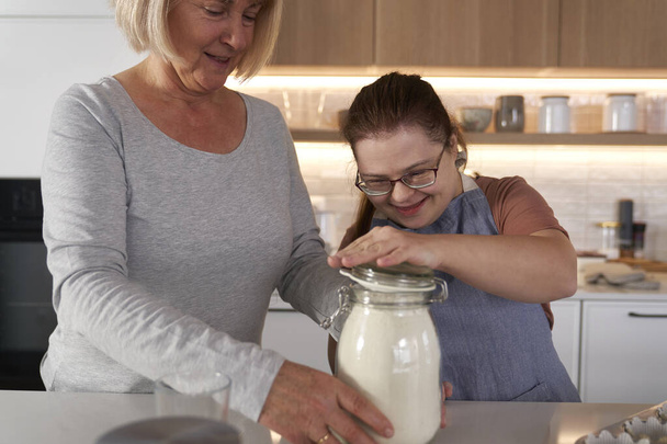 Down-szindrómás nő és az anyja együtt sütnek. - Fotó, kép