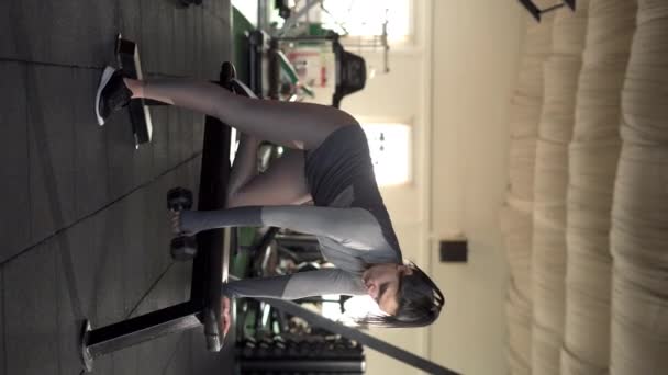 Mladá žena cvičí s činkou na sportovní lavičce v tělocvičně. Koncept síly a motivace. Svislé video - Záběry, video