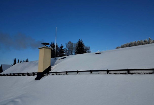 Dumanı tüten bir baca. Ayrıca karlı çatıda kar yağmasını engelleyen bir bariyer var. Metal çubuk katmanı tutar. Bacadaki baca gazını drone ile kontrol etmek çevreyi kurtaracaktır. - Fotoğraf, Görsel