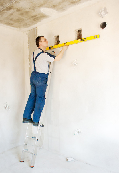 man werknemer controleert de muur met een niveau - Foto, afbeelding