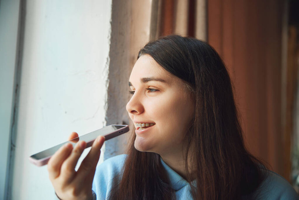 Πορτρέτο της θετικής νεαρή μελαχρινή γυναίκα κάθεται και κοιτάζοντας το παράθυρο, ενώ λαμβάνουν συνομιλία στο τηλέφωνο. Επιλεκτική εστίαση. Έννοια της ομορφιάς και της ιατρικής, επικοινωνία, εργασία σε απευθείας σύνδεση, εκπαίδευση. - Φωτογραφία, εικόνα