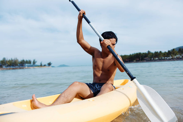 Азиатский мужчина, увлекающийся греблей на байдарках на пляже - Фото, изображение