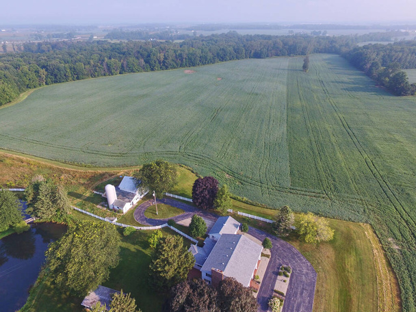 Νωρίς το πρωί εναέρια άποψη ενός γαλήνιου αγροτικού τοπίου με μια πράσινη γεωργική γη, κλασικό λευκό αχυρώνα και ένα όμορφο εξοχικό σπίτι στο Auburn, Ιντιάνα, 2015 - Φωτογραφία, εικόνα