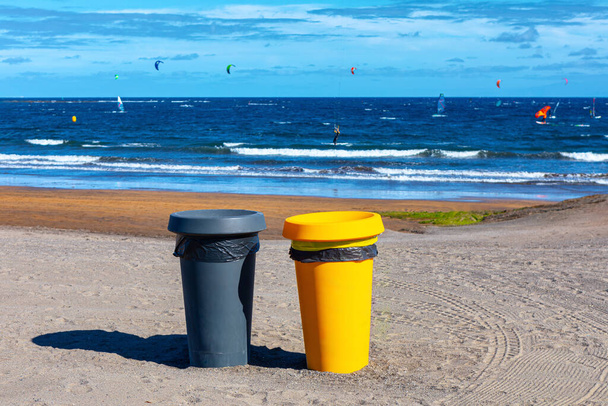 Два пластиковых мусорных бака на песчаном пляже. Мусорные контейнеры на побережье океана  - Фото, изображение