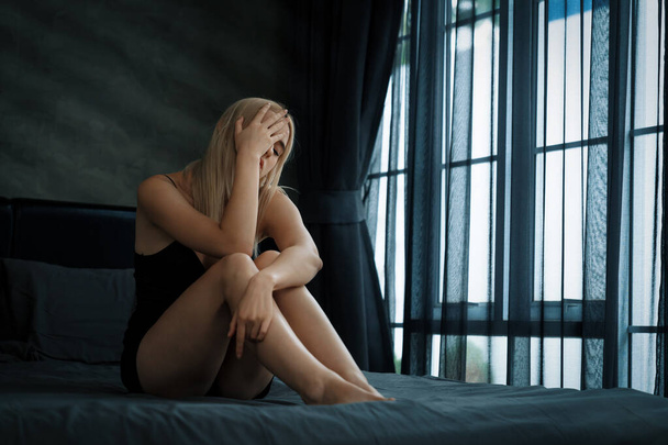 Młoda kobieta z krytyczną depresją i zaburzeniami lękowymi spowodowanymi samotnością, chorobą psychiczną lub niechcianą ciążą, przytulająca się do ciemnej sypialni. Przytłaczająca negatywna myśl. Blithe - Zdjęcie, obraz