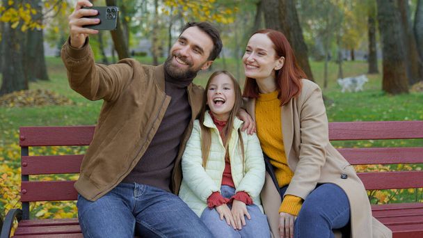 Ευτυχισμένο Καυκάσιο ζευγάρι γονείς μητέρα πατέρας χαριτωμένο κοριτσάκι παιδί κορίτσι λήψη selfie φωτογραφία με κάμερα smartphone χρήση σύγχρονης τεχνολογίας θέτουν σε εξωτερικούς χώρους στο πάρκο τηλέφωνο βίντεο οικογενειακό αρχείο blog vlog - Φωτογραφία, εικόνα