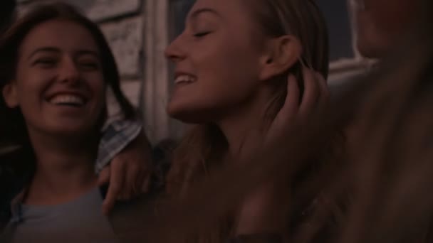 Girl friends sitting in a row during dusk - Materiał filmowy, wideo