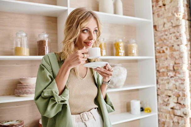Una mujer sosteniendo una taza de café en sus manos en un entorno de cocina. - Foto, Imagen