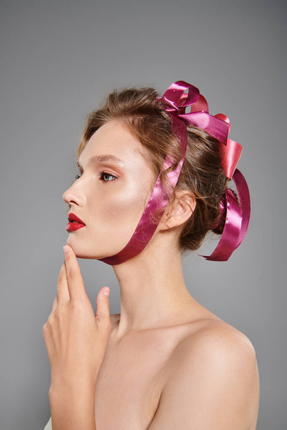 Eine junge Frau mit klassischer Schönheit posiert in einem Studio und strahlt Eleganz aus, während sie eine rosafarbene Schleife auf dem Kopf trägt. - Foto, Bild
