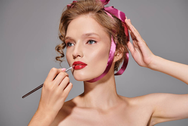 A young woman in a studio setting applies lipstick to her lips, focusing on enhancing her natural beauty. - Photo, Image