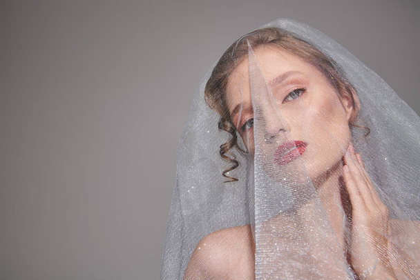 A young woman poses in a studio, wearing a veil on her head, exuding classic beauty and elegance. - Photo, Image