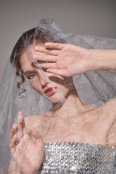 A young woman strikes a pose in a studio, dressed in a wedding gown with a veil gracefully flowing over her head. - Photo, Image
