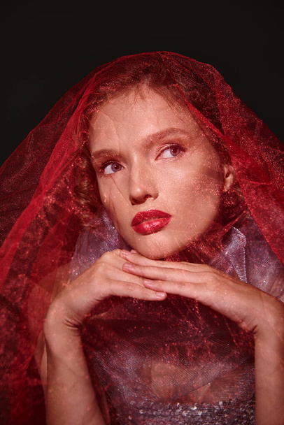 Młoda kobieta emanuje klasycznym pięknem z welonem i odważną czerwoną szminką w studio na czarnym tle. - Zdjęcie, obraz