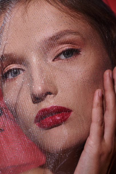 Nuori nainen huokuu klassinen kauneus punainen huulipuna ja huntu peittää kasvonsa, kun hän poseeraa studiossa. - Valokuva, kuva