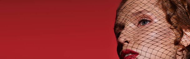 Egy fiatal nő klasszikus szépséget áraszt, miközben feltűnő vörös fátylat visel a fején egy stúdióban.. - Fotó, kép