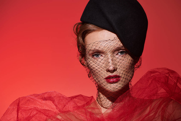 Genç bir kadın, dikkat çekici kırmızı bir elbise ve siyah bir şapkayla klasik bir güzellik sergiliyor.. - Fotoğraf, Görsel