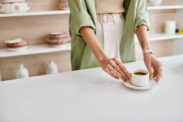 Μια γυναίκα στέκεται σε μια κουζίνα διαμέρισμα, κρατώντας ένα φλιτζάνι καφέ. - Φωτογραφία, εικόνα