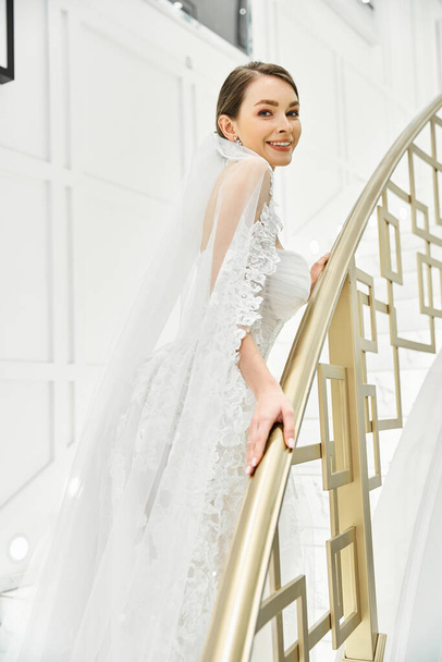 Egy fiatal barna menyasszony menyasszonyi ruhában kecsesen áll a lépcsőn egy menyasszonyi szalonban.. - Fotó, kép