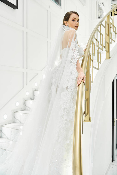 A young brunette bride in a wedding dress stands gracefully on a staircase - Photo, Image