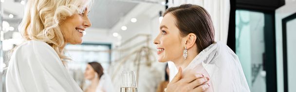 A young brunette bride in a wedding dress stands next to her middle-aged mother in a bridal salon. - Photo, Image