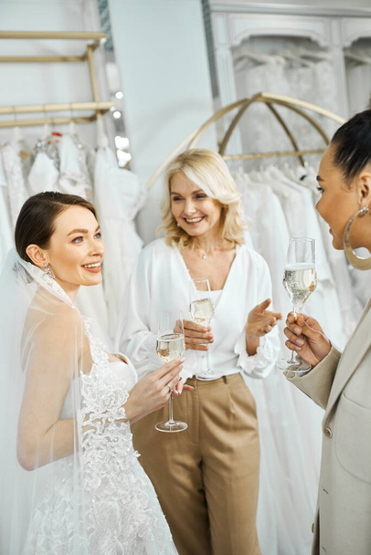 Drei Frauen - eine junge Braut, ihre Mutter mittleren Alters und eine Brautjungfer - stehen nebeneinander und halten jeweils ein Champagnerglas. - Foto, Bild
