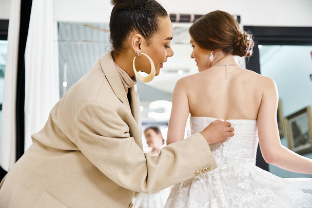 Eine junge brünette Braut im weißen Kleid und eine Brautjungfer im beigen Anzug stehen zusammen in einem Hochzeitssalon und strahlen Eleganz aus. - Foto, Bild