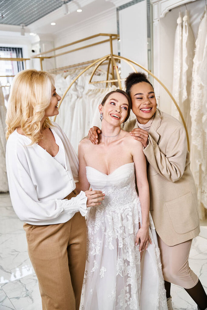 egy fiatal barna és egy gyönyörű menyasszony fehér ruhában, aki kecsesen áll egymás mellett anyával és koszorúslánnyal. - Fotó, kép