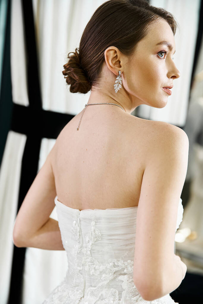Μια νεαρή μελαχρινή νύφη σε ένα λευκό νυφικό θαυμάζοντας την αντανάκλασή της σε έναν καθρέφτη σε ένα σαλόνι γάμου. - Φωτογραφία, εικόνα