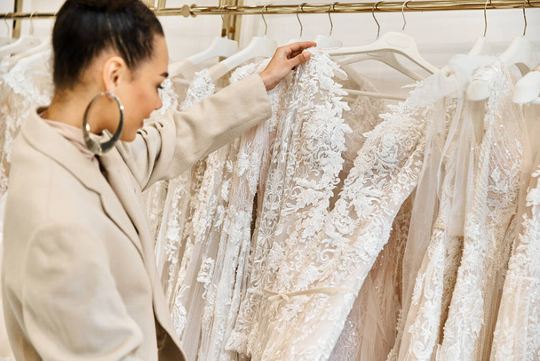Une jeune, belle mariée soigneusement choisir des robes de mariée à partir d'un rack diversifié avec l'aide d'un commerçant. - Photo, image