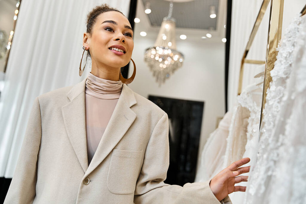 Una giovane bella sposa si trova di fronte a una rastrelliera di vestiti, selezionando attentamente il suo abito da sposa - Foto, immagini
