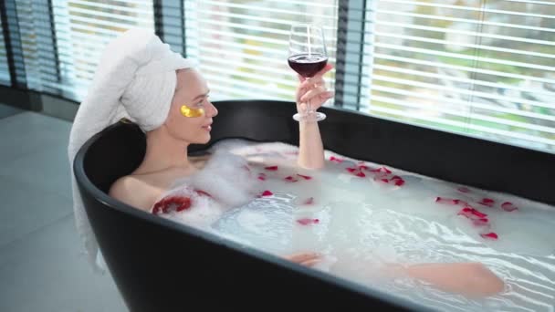 Détente spa. Femme couchée dans le bain avec un verre de vin rouge. Fille se détendre dans la salle de bain à la maison. Jolie femme prenant un bain chaud à boire du vin. Soulagement du stress. Repos après une dure journée de travail - Séquence, vidéo