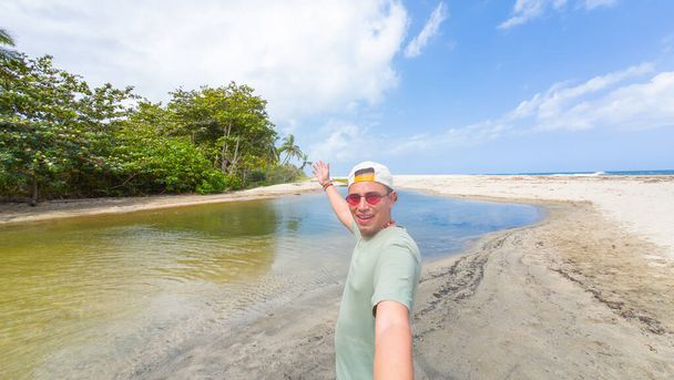 Iloinen mies rento pukea nauttia auringosta rauhallinen rannalla laguuni, vilkuttaa kameralle. - Valokuva, kuva