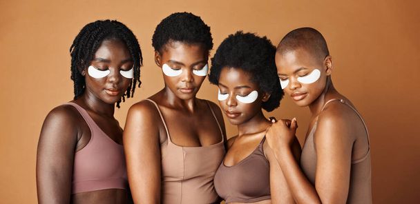 Happy black woman, eye patches and skincare for beauty, epilation or anti aging against a brown studio background. Group portrait of African female people or model in dermatology, health and wellness. - Photo, Image
