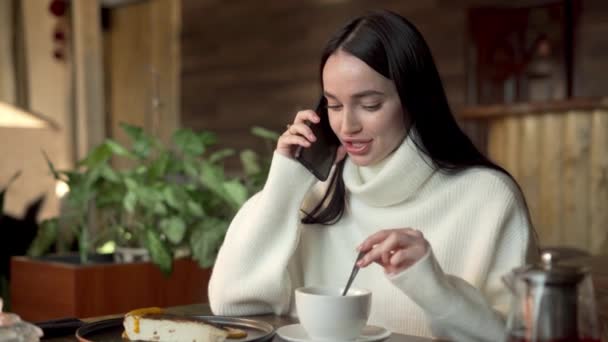 Zaskoczona dziewczyna rozmawiająca przez telefon w kawiarni. Młoda kobieta używa smartfona. Szokujące wieści. Plotkara z szeptem. Przestrzeń kopiowania - Materiał filmowy, wideo