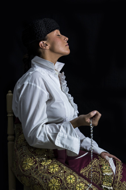 Vrouw stierenvechter in kapel met rozenkrans bidden op haar hand op een zwarte achtergrond - Foto, afbeelding